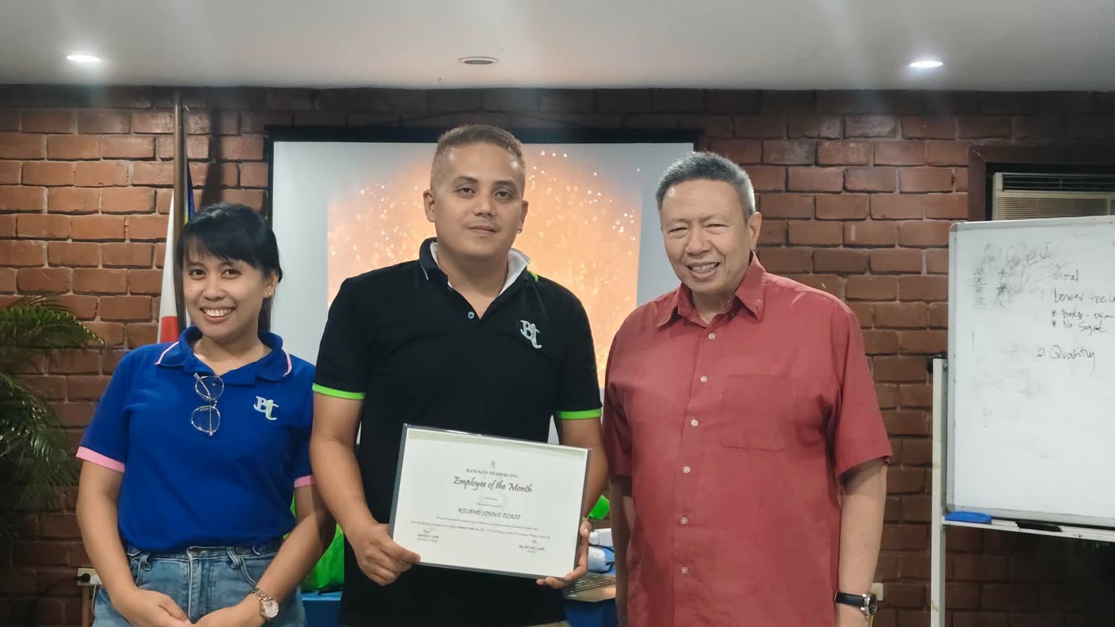 Roland John receiving the Employee of the Month certificate beside a colleague and the company president